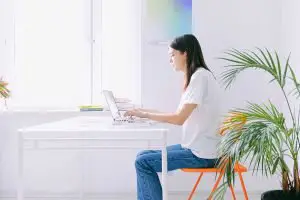 white home office with white desk, orange chair and woman.
