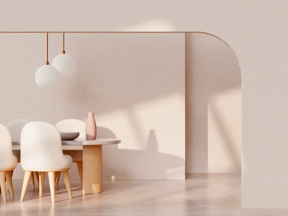 Minimalist dining room with a light wood table, four white cushioned chairs, and pendant lights—showing how to make your living space feel more high-end without a full renovation. Soft sunlight casts shadows on the arched wall and floor.