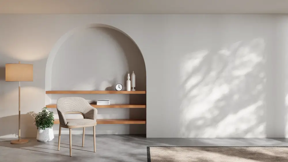 A minimalist living space with a beige armchair, floor lamp, potted plant, and arched wall niche featuring wooden shelves shows how to make your living space feel more high-end without a full renovation. Sunlight casts soft shadows on the white wall.